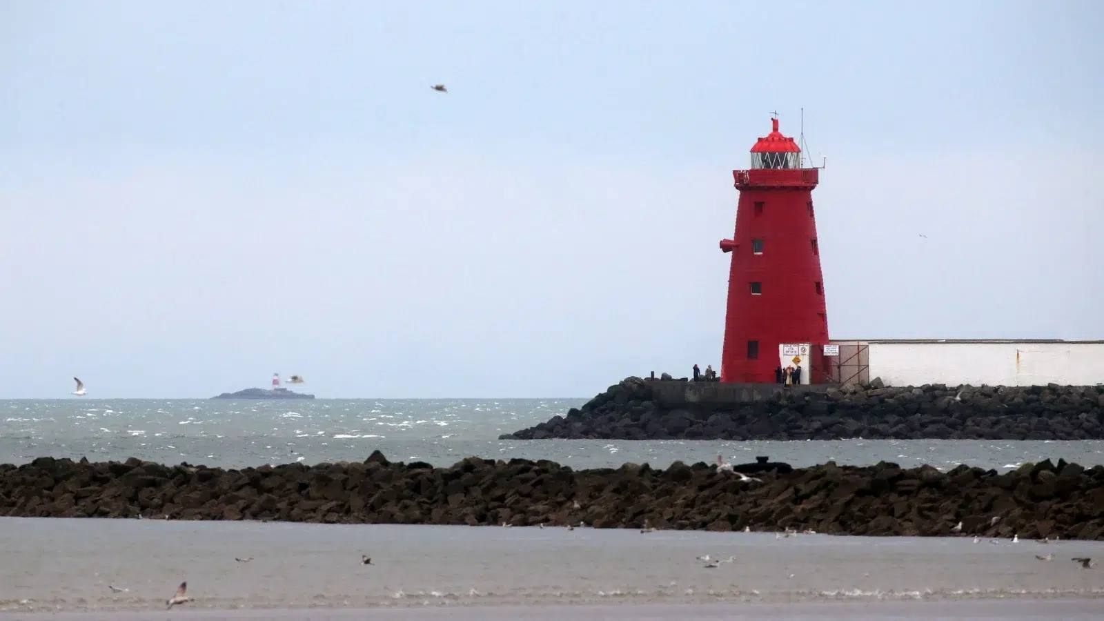 A red lighthouse expertly sits on a beach near a body of water.