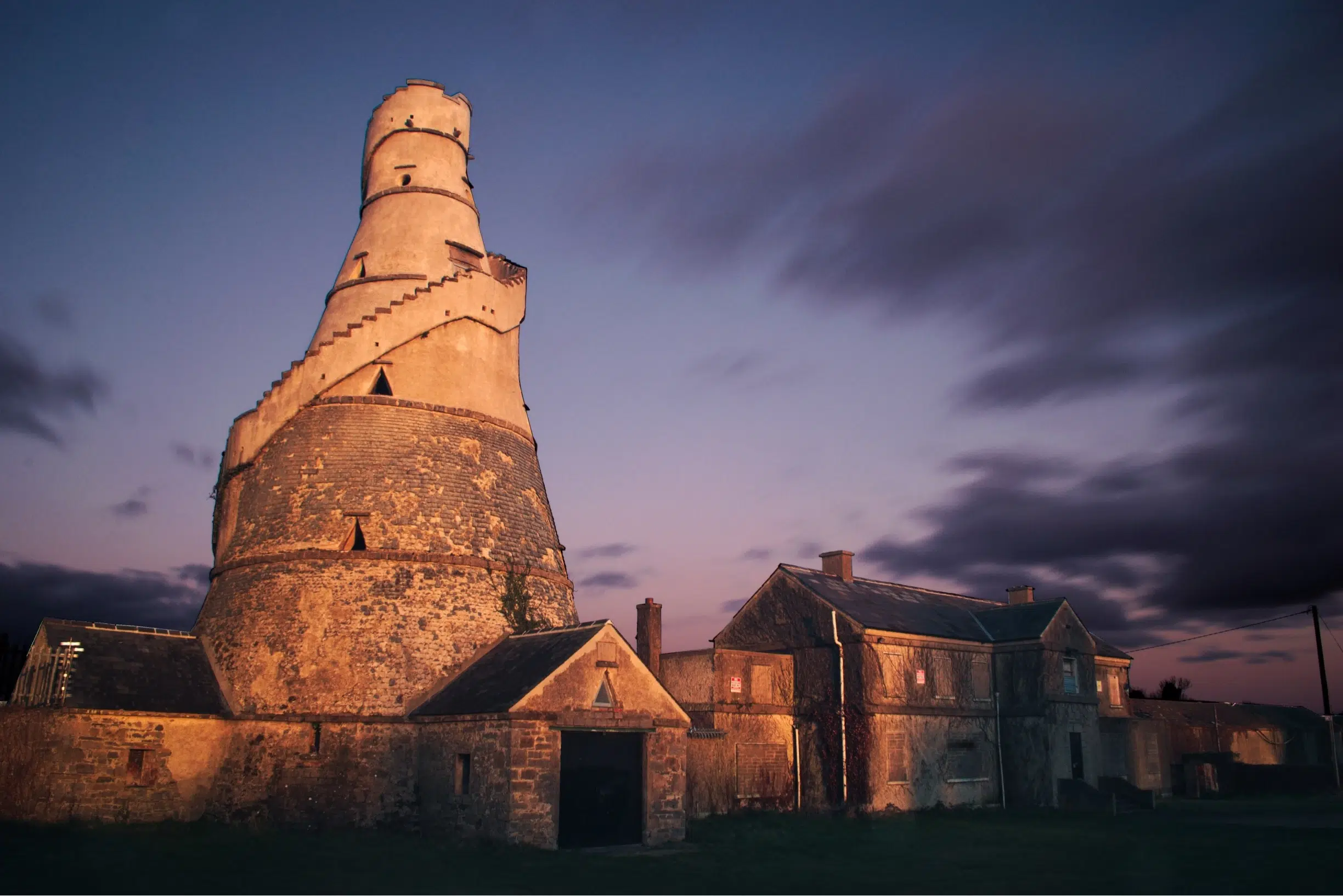 An expertly crafted old stone tower stands majestically in the middle of a picturesque field at dusk.