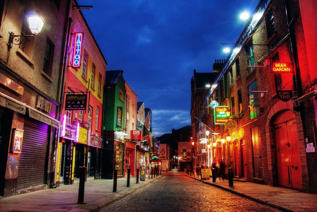 A bustling city street at night, illuminated by the glow of streetlights and the occasional passing car.