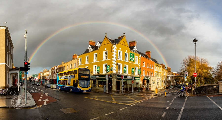 An expert removals double decker bus with a rainbow in the sky.